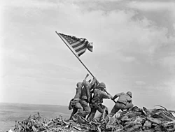 Soldiers raising a U.S. flag on a rocky hilltop